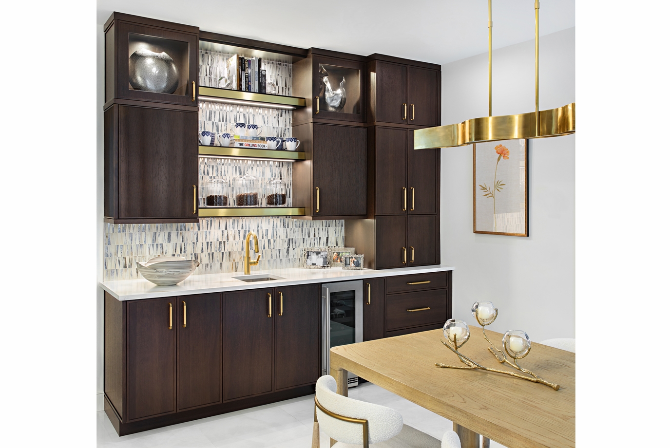 In the bar area, sleek metal-edged shelves are paired with a mixed-finish mosaic glass backsplash, creating a captivating play of light and texture. The metallic details frame the display beautifully, while the shimmering glass tile adds a layer of depth and glamour - perfect for entertaining.